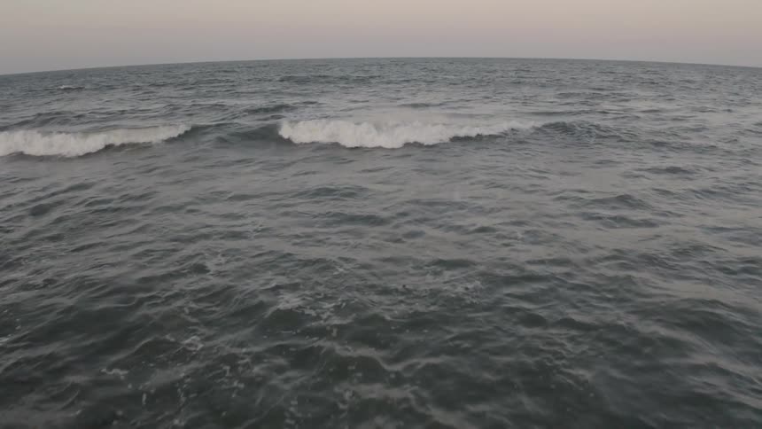 Waves crash on the open ocean under a cloudy sky