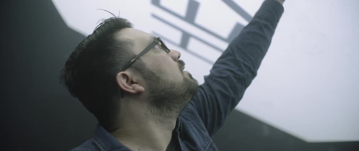 A man that is pointing at a screen on the ceiling