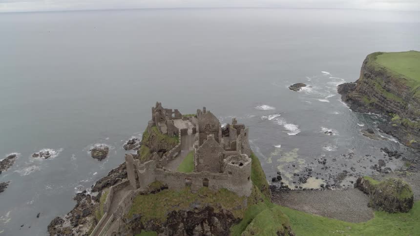 A castle on the edge of the sea surrounded by fields and slopes of green grass and moss