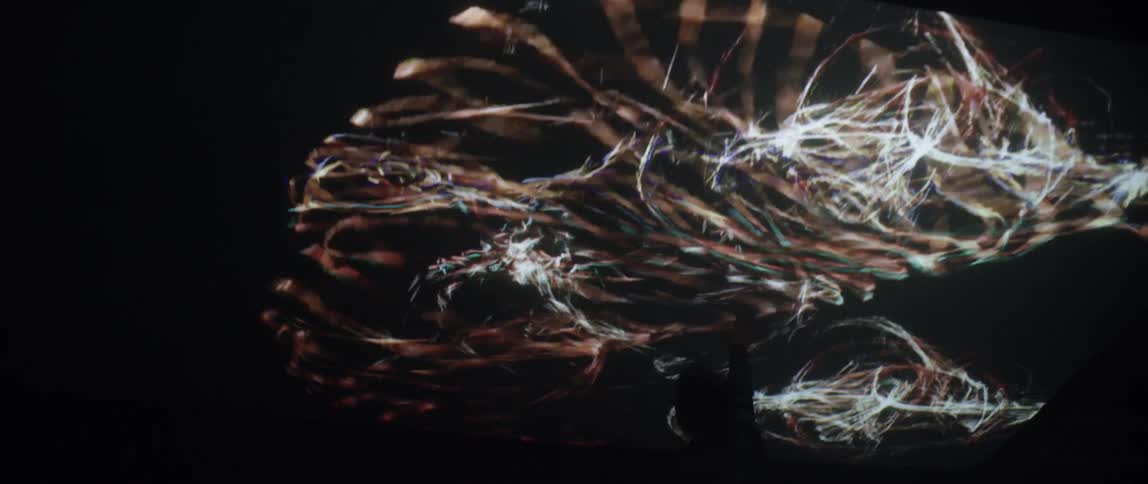 A man touches an enormous television screen displaying bright and colorful visuals