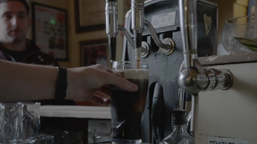 A bartender pours a glass of beer from a tap