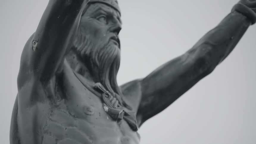 The statue of a man wearing a crown and cape over a bare chest with arms raised to the sky