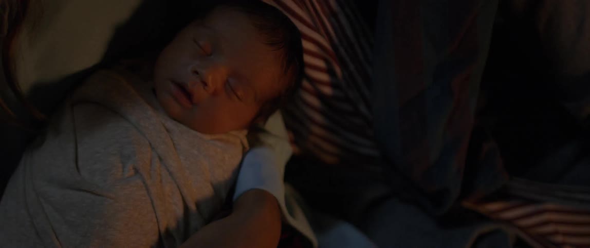 A newborn baby is tightly wrapped up warm in the arms of its mother at night