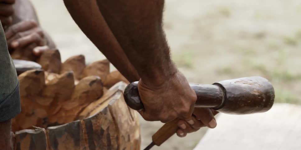 A man bangs a chisel with a mallet against a piece of wood