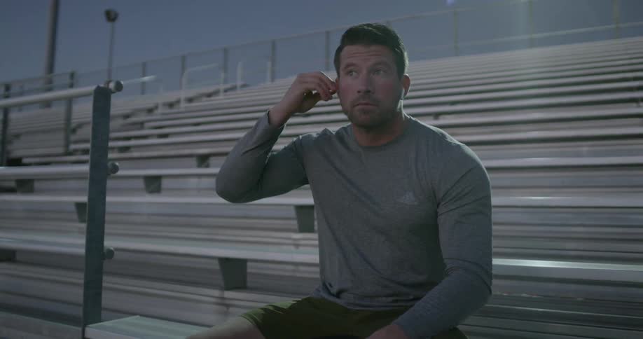 A young man puts earbuds in as he sits in the bleachers