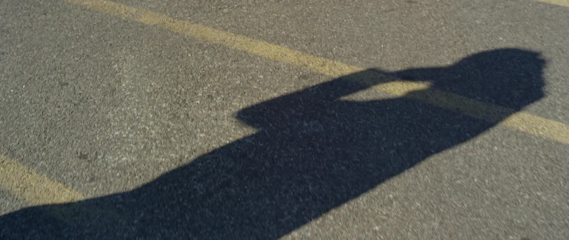 The shadow of a man walking across a street while putting on a cap