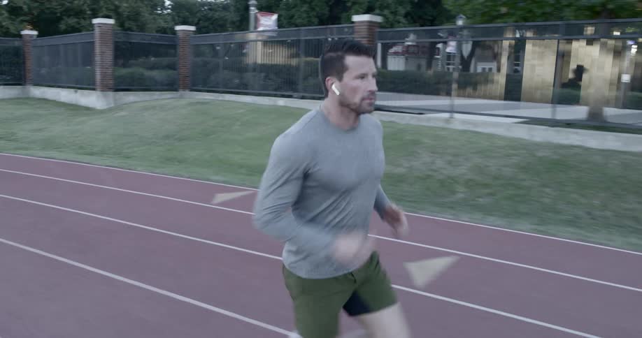 A man running on an outdoor track while wearing headphones