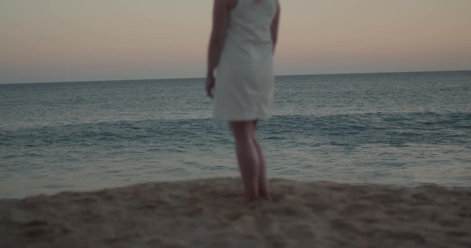 A white woman in a white dress stands on a beach