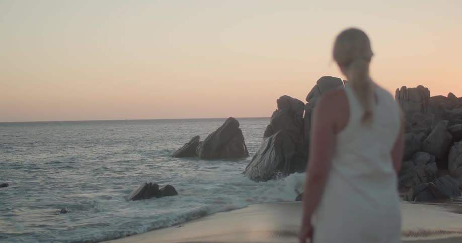 A woman stands on the beach looking out at the water