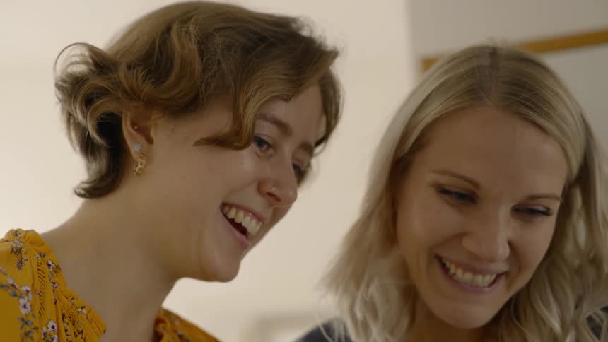 Two women laughing while flipping through things on a cell phone
