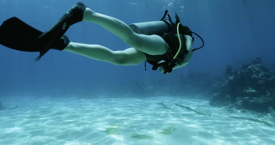 A woman scuba diving in clear ocean water near a reef