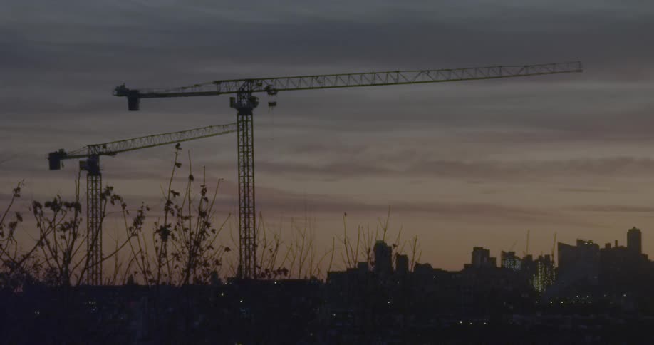Two cranes with a city skyline in the background