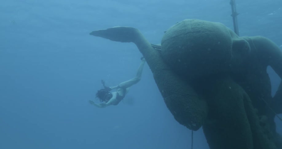 Woman snorkels around underwater statue