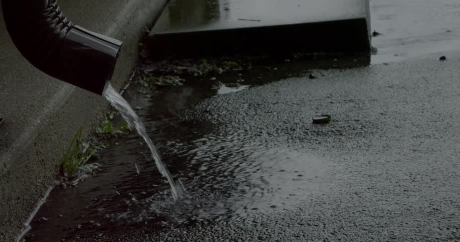 Rainwater from a drainage is falling on asphalt
