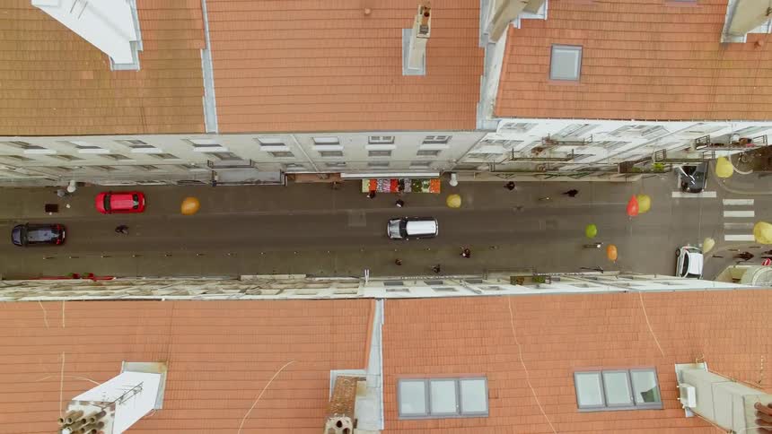 People and cars travel on a street between apartment buildings with balloons hanging in the air above them