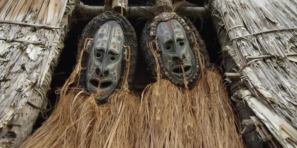 Painted masks decorated with grass hang in a hut