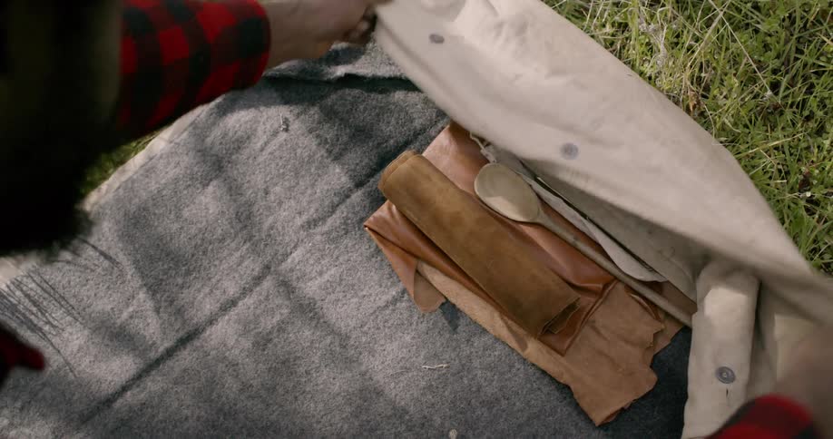 A man rolls out a bedroll in the grass