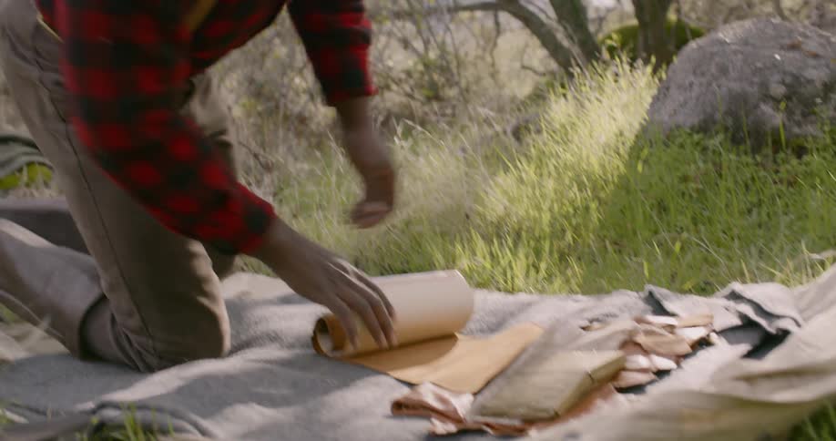 A man rolls out his sleeping bag near a rock