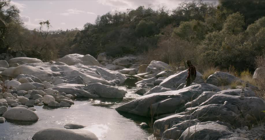 A man walks on rocks next to a river