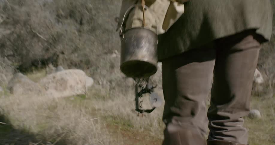 A man walking down an outdoor trail carrying hunting and cooking gear