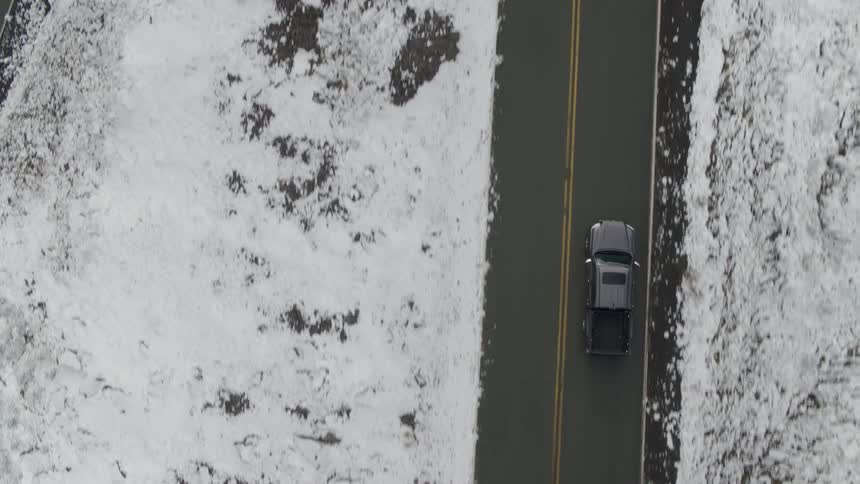 An aerial view of a truck driving on a road on a snowy day