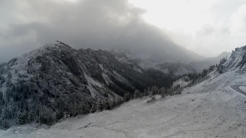 Steep mountains and tall fir trees covered in snow with a clear mountain road through the valley
