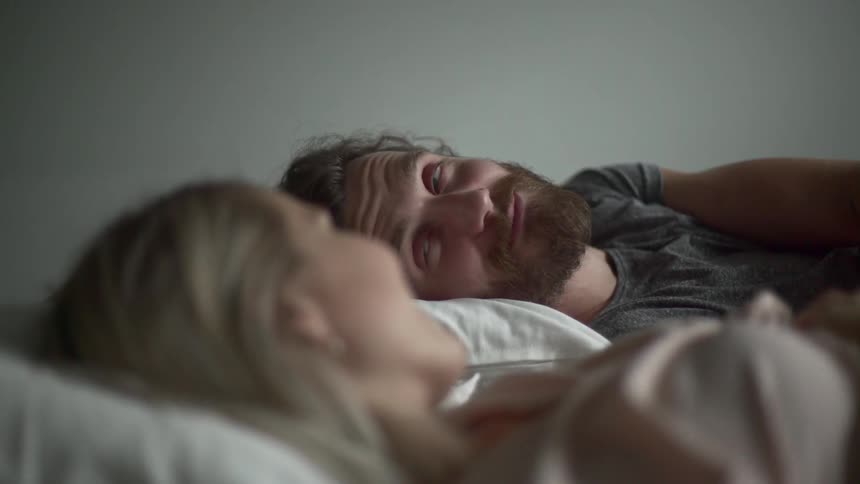 A man shows a big grin to a woman laying next to him