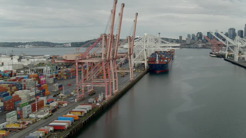 A shipping container port with a large ship cranes and thousands of containers near a city skyline