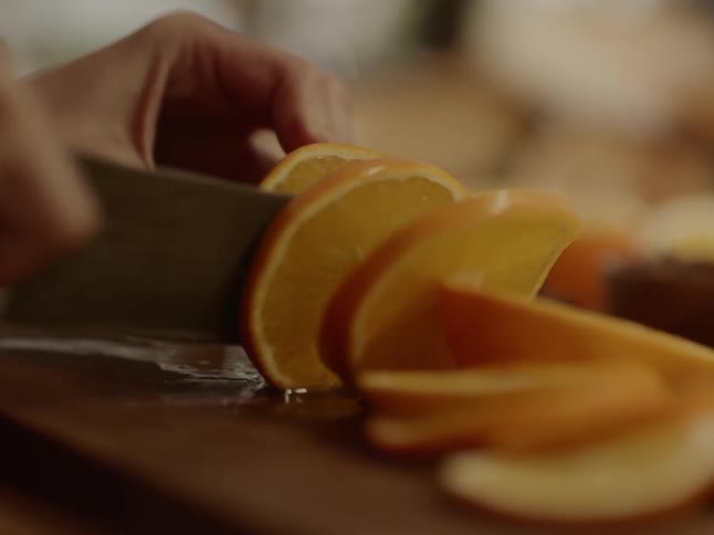 An orange being sliced on a wooden cutting board