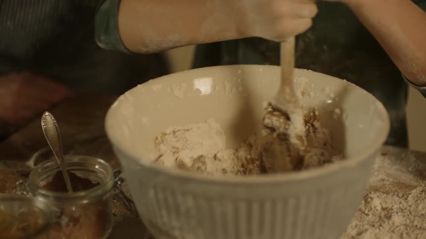 A child uses a wood spoon to stir dough in a ceramic bowl