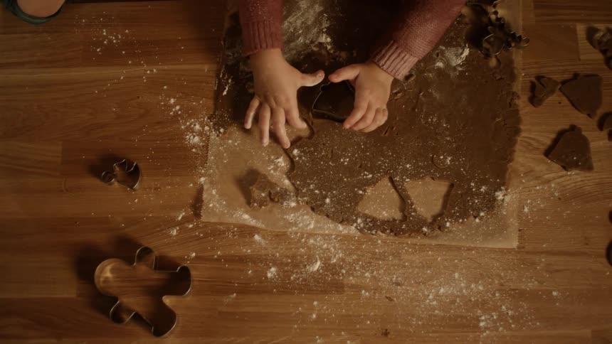 A child uses a cookie cutter to make cookies with an adult