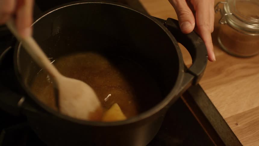 A white person stirs a broth with a wooden spoon