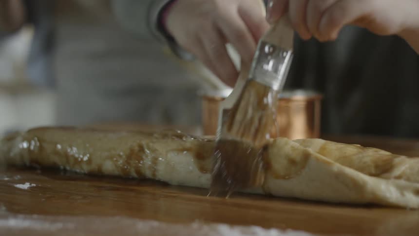 A child paints dough with batter using a paint brush in each hand