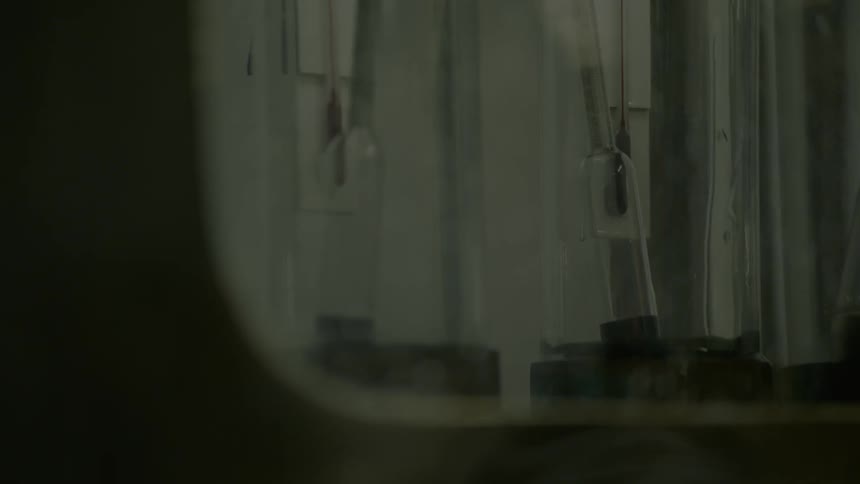 A person turns a dial as fluid rises in tubes behind glass