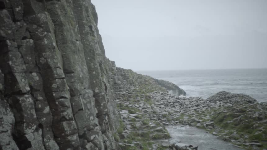 Waves crash and splash on shore at the base of a rocky cliff