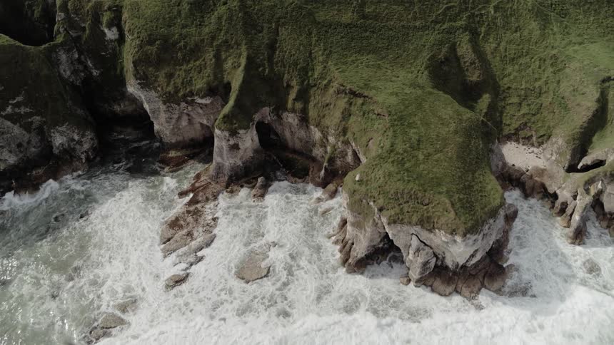 Car driving along cliff road as waves crash against shore