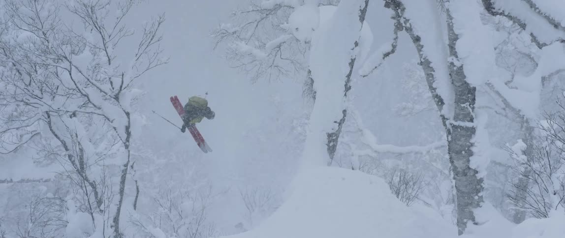 Man skiing and jumping downhill through a forest