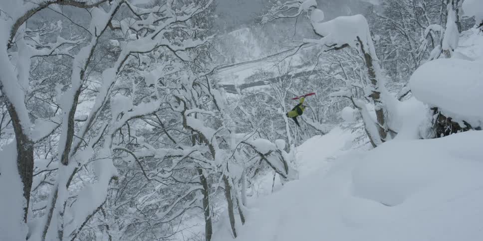 A skier jumps down a cliff while doing a backflip
