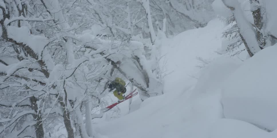 Skier making leap down slope while another films