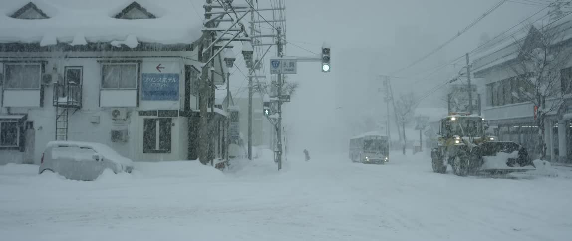 Snow plow and bus crossing intersection during snow storm