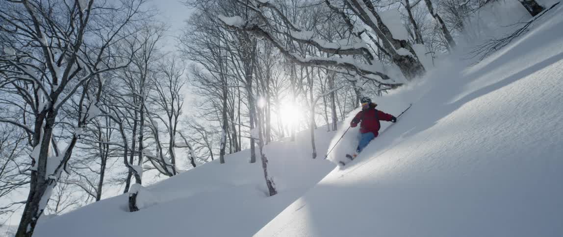 A skier rides down a steep slope full of powder