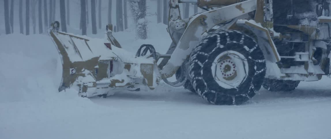 A cat snow plough attempts to clear a path under heavy snowfall