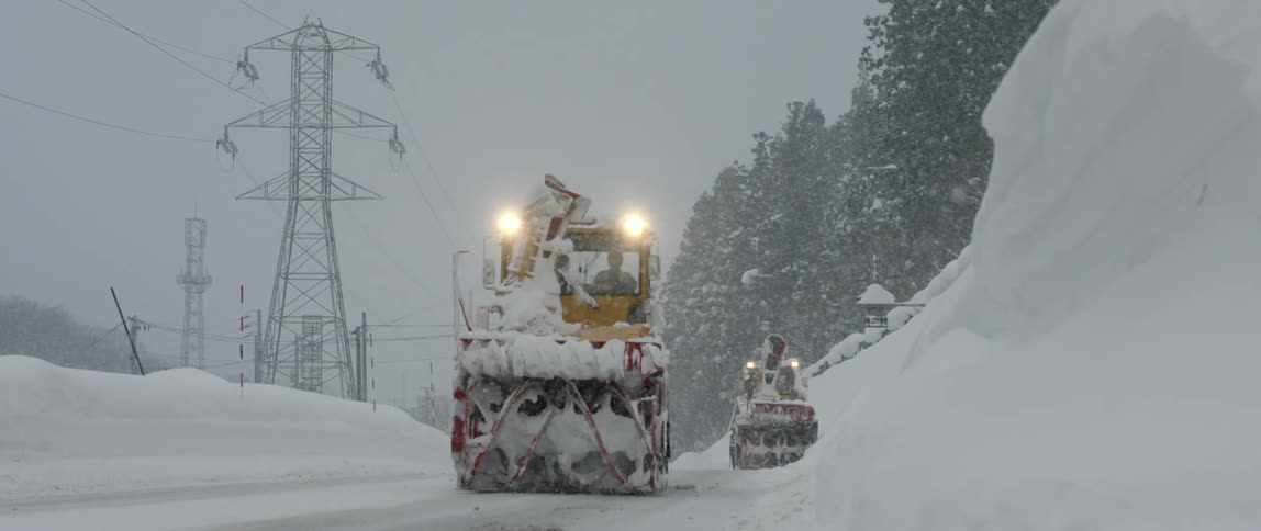 Snowplows driving down a road on a snowy day