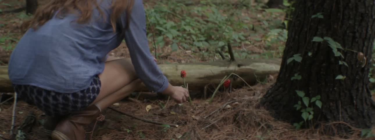 A woman hikes across a trail and picks a red flower