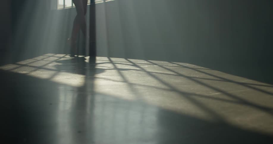 A dancer in a dim room practicing by a window
