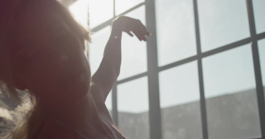 A woman does ballet movements while standing next to a large window in a dance studio