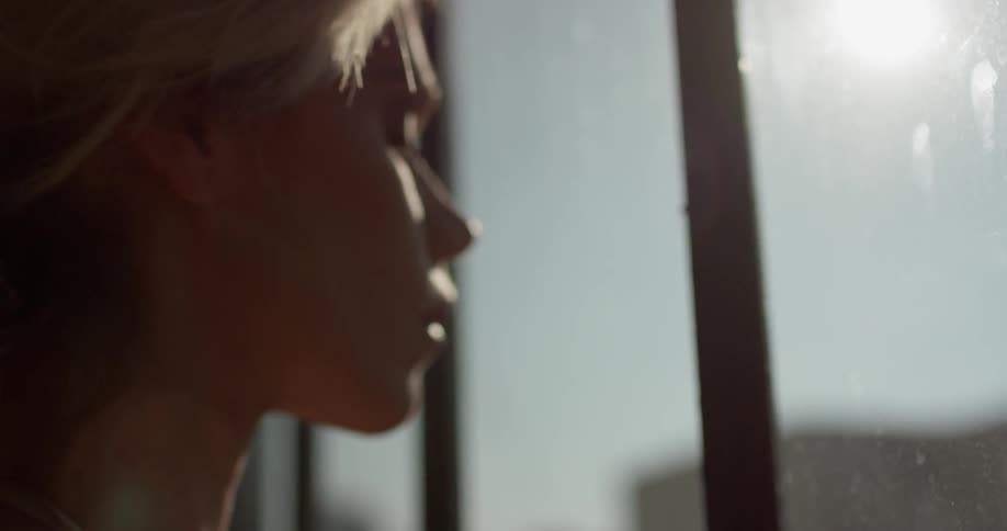 A white woman stands in a room and looks out a window