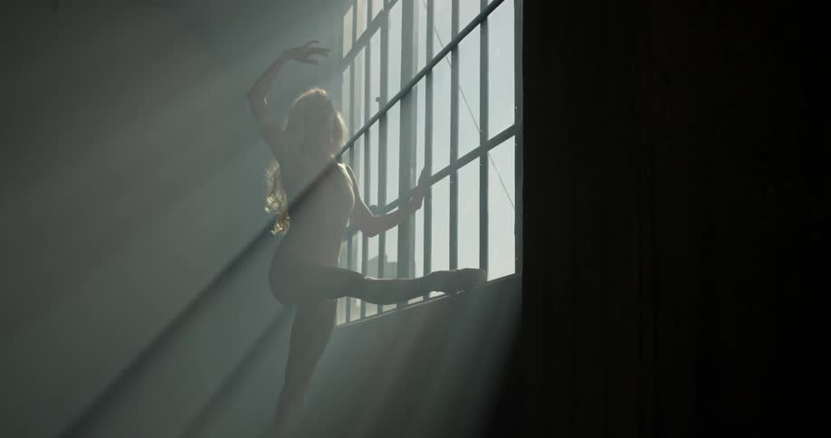 A woman practices ballet at the window sill in a dance studio