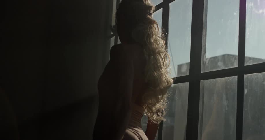 A woman practices ballet moves while standing next to a window in a dance studio