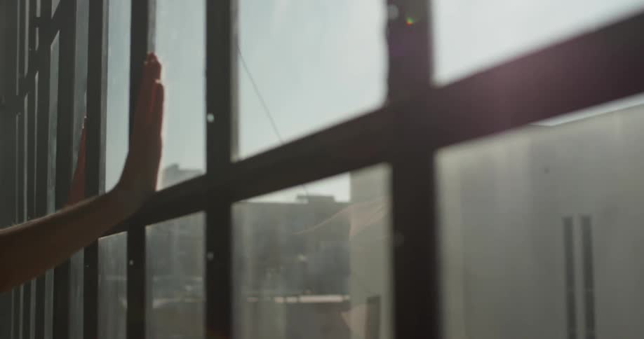 Person seen in window reflection puts hands on window pane